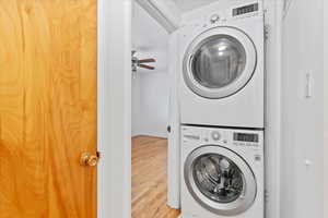 Clothes washing area with laundry area, wood finished floors, ceiling fan, and stacked washer and dryer