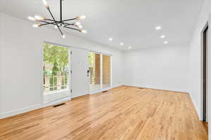 Unfurnished room featuring an inviting chandelier, light wood-type flooring, visible vents, baseboards, and recessed lighting