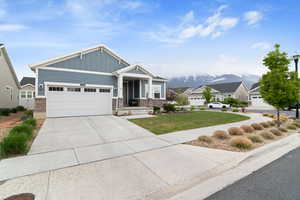 Craftsman-style house with board and batten siding, an attached garage, concrete driveway, a front lawn, and a mountain view