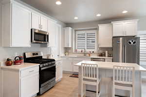 Kitchen with appliances with stainless steel finishes, a sink, white cabinetry, light wood-type flooring, and recessed lighting