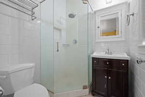 Bathroom featuring tile walls, toilet, a stall shower, and vanity