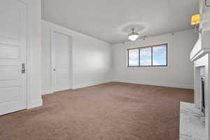 Unfurnished living room with a fireplace with flush hearth, carpet floors, and baseboards