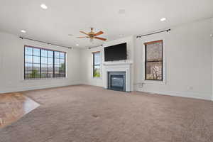Unfurnished living room with a ceiling fan, a fireplace with flush hearth, baseboards, light colored carpet, and recessed lighting