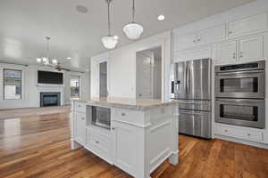 Kitchen with stainless steel appliances, wood finished floors, pendant lighting, an inviting chandelier, and white cabinets