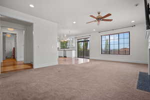 Unfurnished living room with light colored carpet, baseboards, ceiling fan with notable chandelier, and recessed lighting