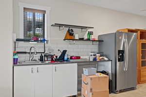 Kitchen with tasteful backsplash, a sink, stainless steel fridge, open shelves, and white cabinets