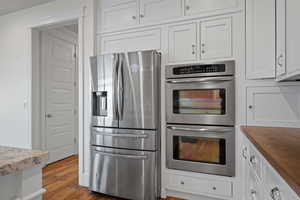 Kitchen with stainless steel appliances, white cabinetry, and wood finished floors