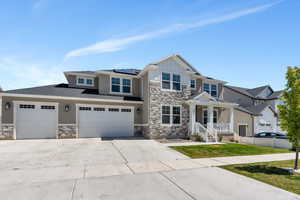 Craftsman house featuring stone siding, concrete driveway, roof mounted solar panels, and board and batten siding
