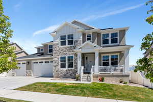 Craftsman-style home featuring a porch, stone siding, concrete driveway, a front yard, and board and batten siding