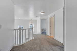 Corridor with light colored carpet, a textured ceiling, an upstairs landing, a chandelier, and baseboards