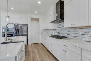 Kitchen featuring stainless steel appliances, wall chimney range hood, light wood-type flooring, recessed lighting, and white cabinetry