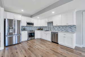 Kitchen with a sink, stainless steel appliances, white cabinetry, and light wood-style floors