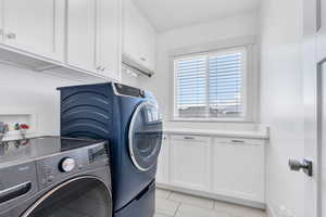 Washroom with cabinet space, washing machine and clothes dryer, and light tile patterned flooring