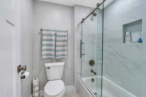 Full bathroom featuring toilet, shower / bath combination with glass door, and baseboards