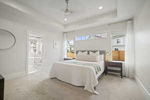 Bedroom with ensuite bath, recessed lighting, light carpet, a raised ceiling, and baseboards