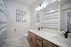 Full bath with a sink, double vanity, toilet, and baseboards