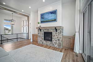 Living room featuring wood finished floors, a chandelier, recessed lighting, and a stone fireplace