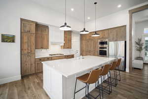 Kitchen with appliances with stainless steel finishes, decorative backsplash, brown cabinetry, and light wood-style floors