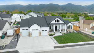 Modern farmhouse with stone siding, an attached garage, roof with shingles, a porch, and a residential view
