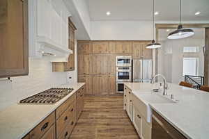 Kitchen with a sink, stainless steel appliances, decorative light fixtures, backsplash, and light wood-style floors