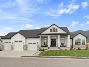 View of front of property with board and batten siding, stone siding, a porch, an attached garage, and a front yard
