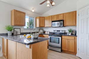 Kitchen featuring appliances with stainless steel finishes, a peninsula, lofted ceiling, light wood-type flooring, and ceiling fan