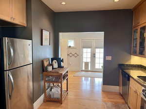 Kitchen featuring recessed lighting, light wood finished floors, glass insert cabinets, baseboards, and appliances with stainless steel finishes