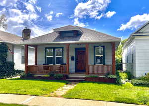 View of front facade featuring covered porch, roof with shingles, and a front yard