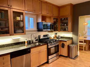 Kitchen with light wood-style floors, dark stone countertops, appliances with stainless steel finishes, and a sink