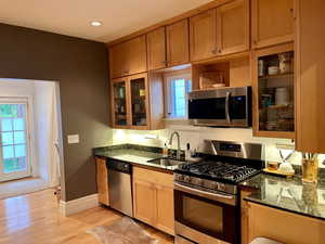Kitchen with a sink, dark stone countertops, glass insert cabinets, baseboards, and appliances with stainless steel finishes