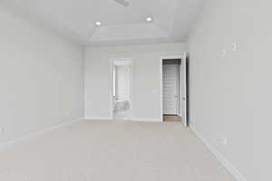 Unfurnished bedroom with recessed lighting, a tray ceiling, light carpet, connected bathroom, and baseboards