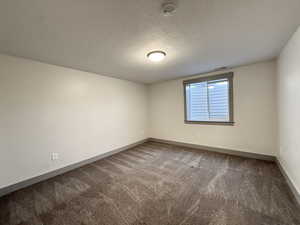 Spare room featuring a textured ceiling, carpet floors, baseboards, and visible vents