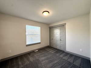 Unfurnished bedroom featuring a closet, visible vents, baseboards, and dark carpet