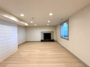 Unfurnished living room featuring baseboards, light wood-type flooring, a tiled fireplace, and recessed lighting