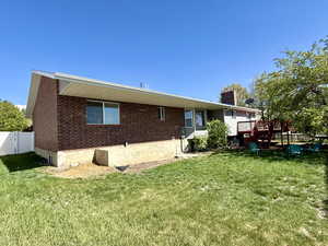 Rear view of property with a lawn, a chimney, fence, and a deck