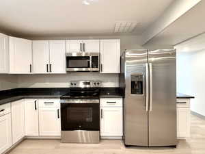 Kitchen with white cabinets, light wood-style floors, stainless steel appliances, and visible vents