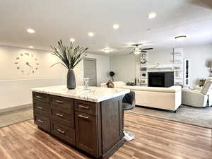Kitchen with dark brown cabinetry, ceiling fan, a kitchen breakfast bar, and light wood-style floors