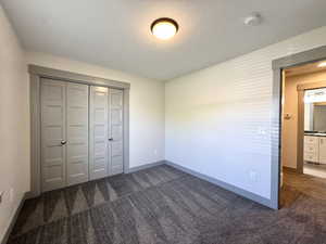 Unfurnished bedroom with baseboards, a closet, dark colored carpet, and a textured ceiling