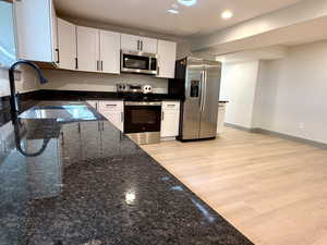 Kitchen with recessed lighting, a sink, white cabinetry, stainless steel appliances, and dark stone counters