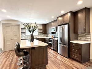 Kitchen featuring dark brown cabinets, open shelves, a kitchen breakfast bar, light wood-style floors, and stainless steel appliances