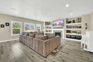 Living room with light wood-style flooring, a fireplace, baseboards, and recessed lighting