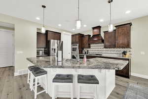 Kitchen with appliances with stainless steel finishes, custom range hood, baseboards, dark brown cabinetry, and recessed lighting
