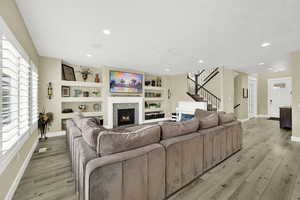 Living area with baseboards, stairs, light wood finished floors, a tile fireplace, and recessed lighting