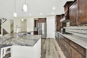 Kitchen featuring stainless steel appliances, a sink, a breakfast bar, light wood-style flooring, and tasteful backsplash
