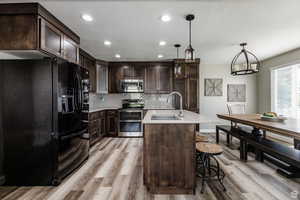 Kitchen with appliances with stainless steel finishes, a sink, dark brown cabinets, light countertops, and light wood-type flooring