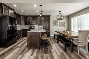 Kitchen with stainless steel appliances, light wood-style floors, dark brown cabinetry, a sink, and light countertops