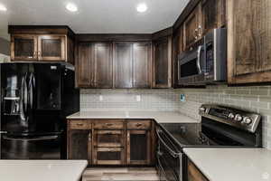 Kitchen with appliances with stainless steel finishes, dark brown cabinetry, light countertops, decorative backsplash, and a textured ceiling