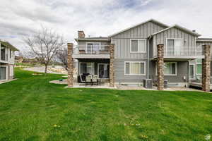 Back of property with a balcony, board and batten siding, a patio, a chimney, and a lawn