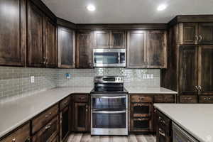 Kitchen featuring stainless steel appliances, light wood-style floors, light countertops, dark brown cabinets, and tasteful backsplash