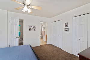 Carpeted bedroom with two closets, baseboards, connected bathroom, and a ceiling fan